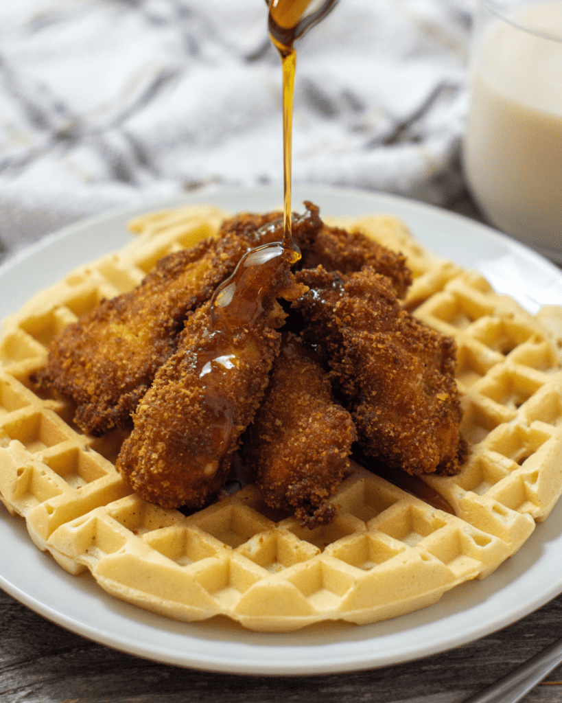 Chicken and Waffles on a plate being drizzled with maple syrup.