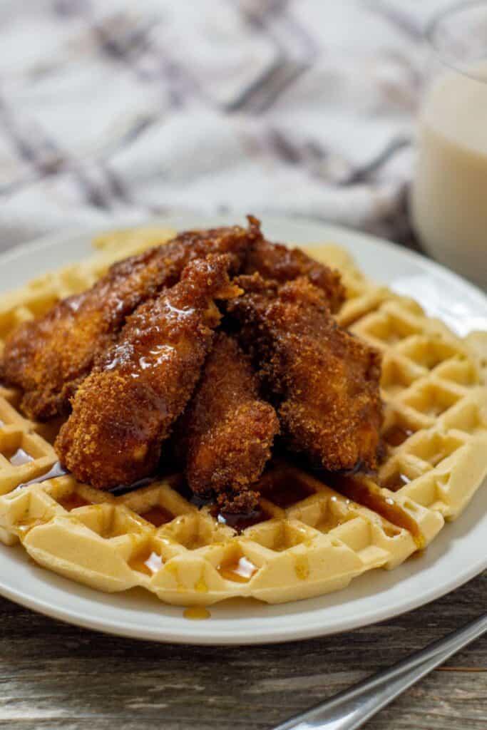 Chicken and Waffles on a plate drizzled with maple syrup.