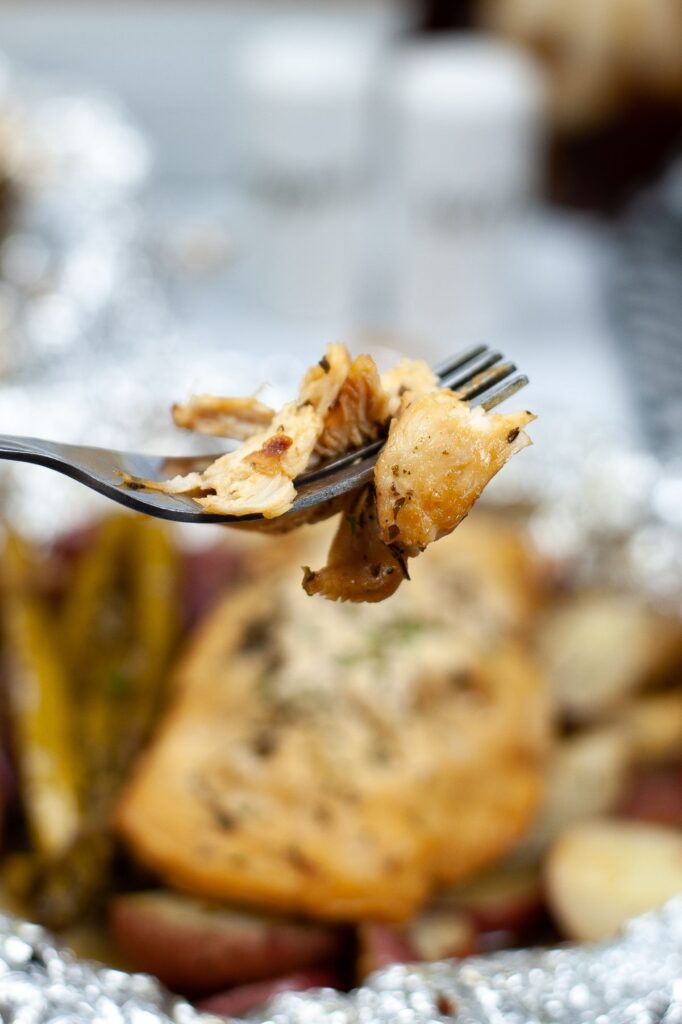 closeup of a piece of Honey Garlic Chicken on a fork with the rest of the foil packet blurred in the background.