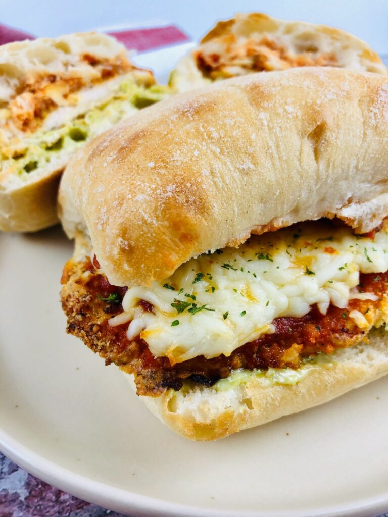 Chicken Parmesan Sandwich on a plate and the other sandwich is cut in half.