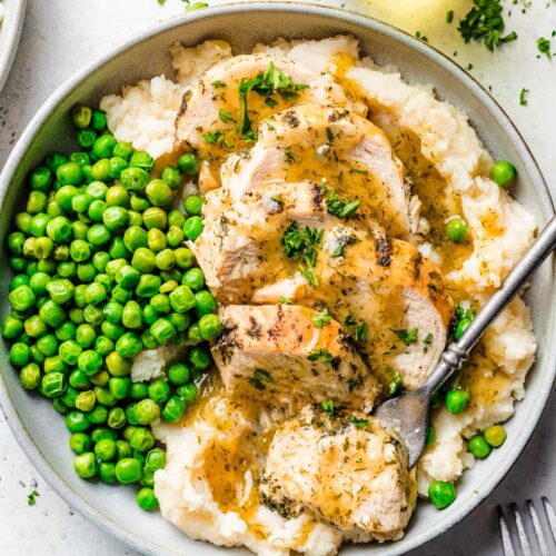 chicken breasts topped with gravy alongside peas