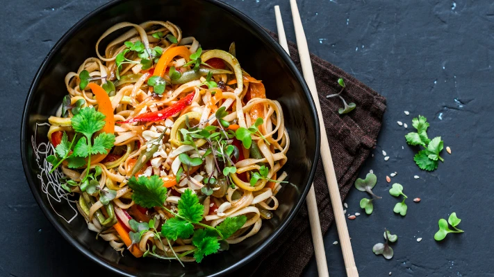 chicken noodles and vegetables in a pan alongside chop sticks