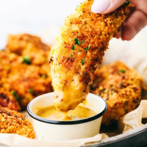a hand dipping crispy chicken tender in sauce