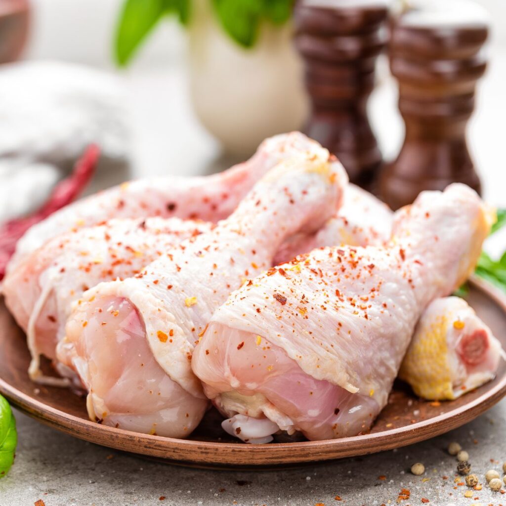 closeup of seasoned uncooked chicken legs on a brown plate.